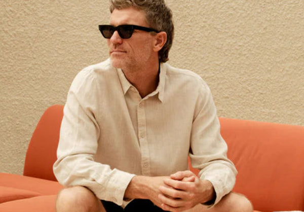 Man sitting on a red couch wearing sunglasses and casual clothing.
