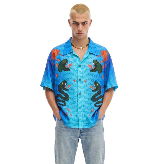 Person wearing a blue patterned shirt with hands in pockets on a white background